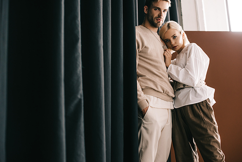 stylish couple standing near curtain and  on brown