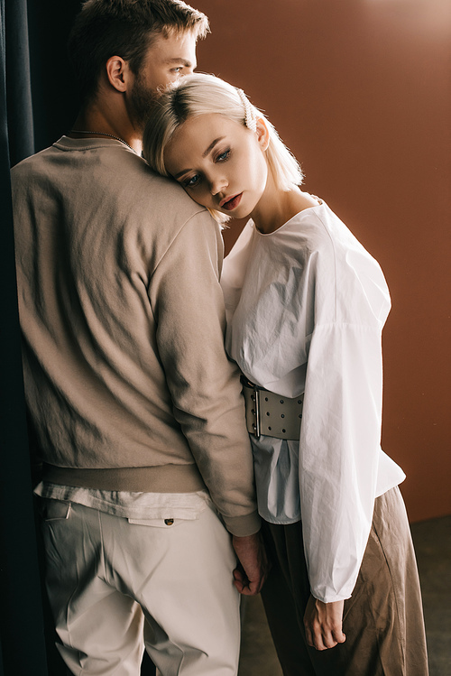 stylish couple standing near curtain and looking away on brown