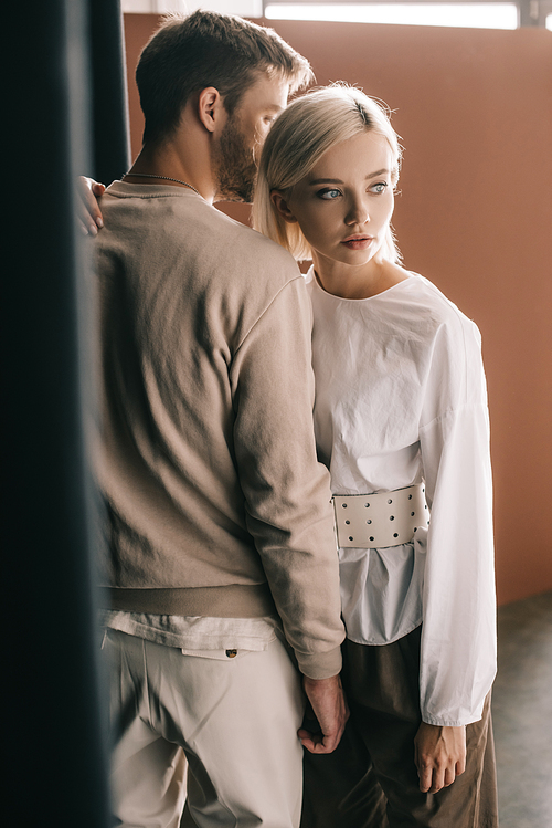 stylish couple standing near curtain and looking away on brown