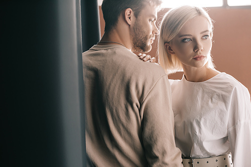 stylish couple standing near curtain and looking away