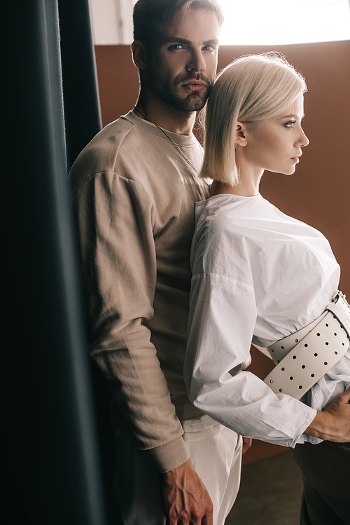 stylish couple standing near black curtain on brown