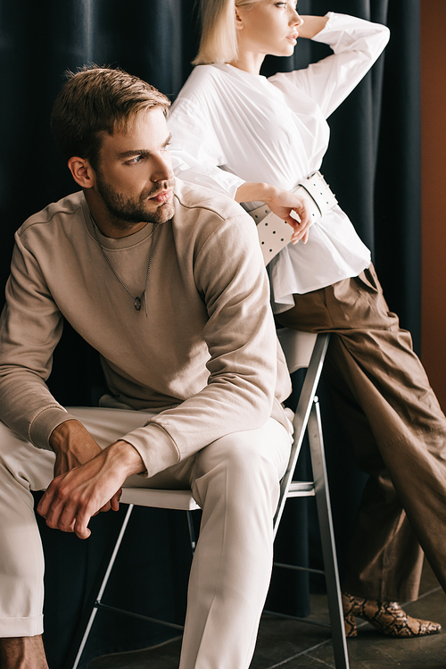 cropped view of woman in white blouse and bearded man sitting on chair near curtain