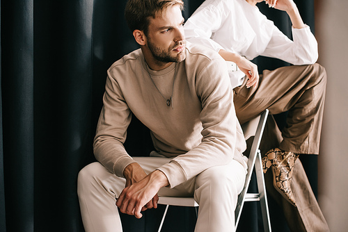 cropped view of woman in white blouse and bearded man sitting on chair near curtain