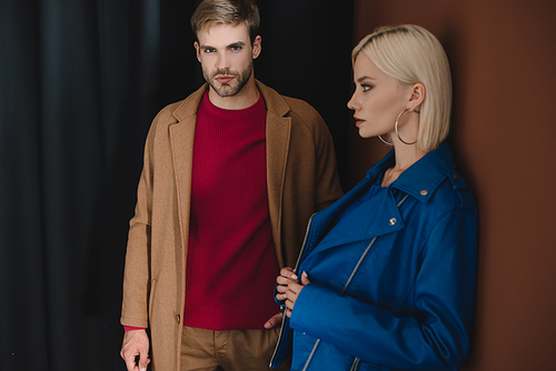 stylish couple in autumn outfits standing near curtain