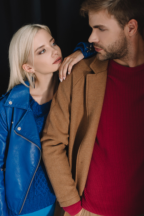 blonde girl and bearded man in autumn outfits looking at each other on black