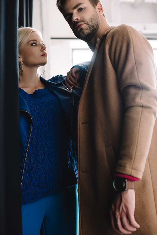 stylish young woman and man in autumn clothes near black curtain