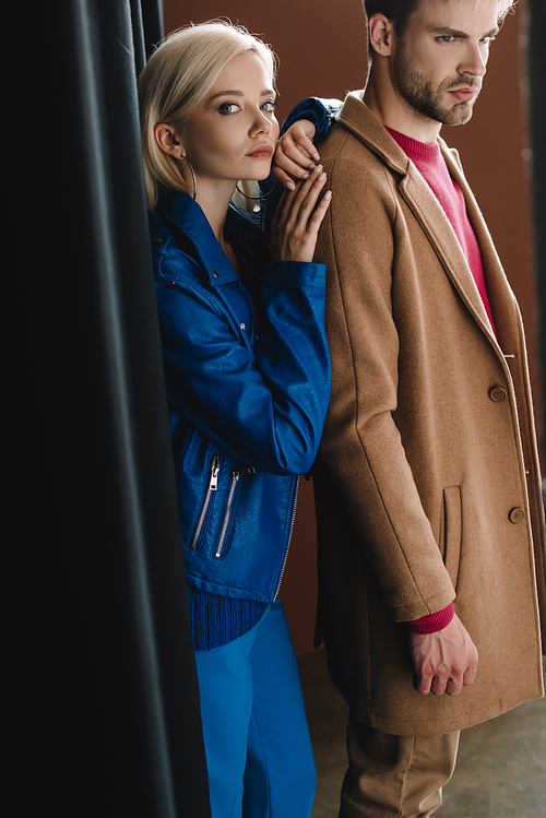 stylish young woman and man in autumn clothes near black curtain