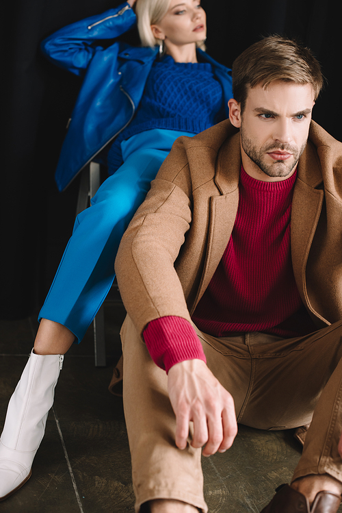 stylish young woman and man in autumn clothes near black curtain