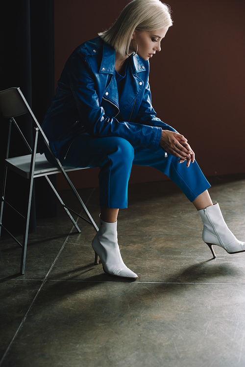 attractive blonde woman wearing leather jacket and heels sitting on chair