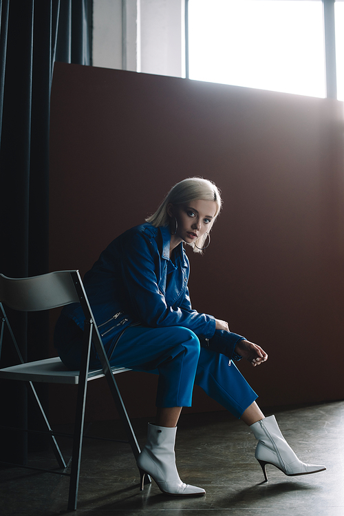 attractive blonde woman wearing leather jacket and heels sitting on chair and 