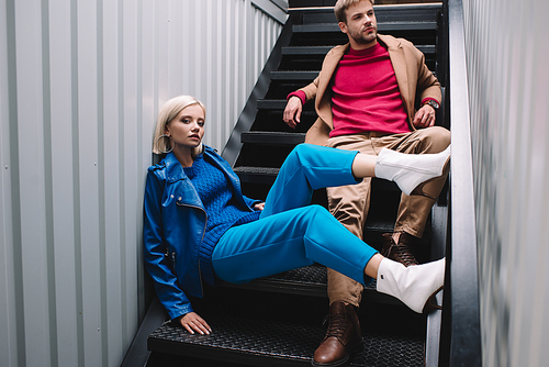 stylish young woman and man in autumn clothes sitting on stairs