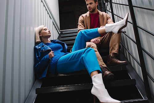 stylish young woman and man in autumn clothes sitting on stairs