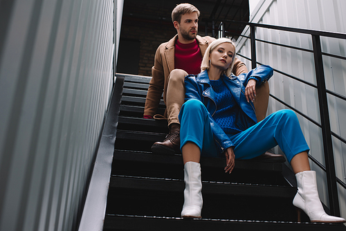 bottom view of stylish young woman and man in autumn clothes sitting on stairs