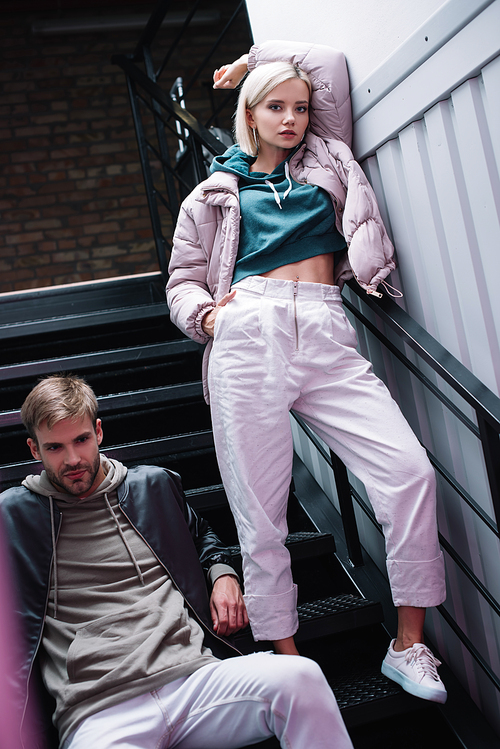 stylish young man and woman in casual autumn outfits on stairs