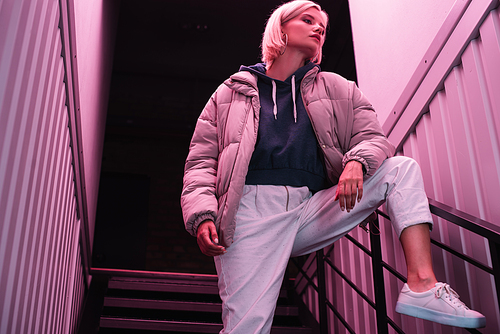 blonde young woman in down jacket on stairs