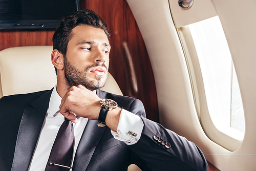 handsome businessman in suit looking through window in private plane