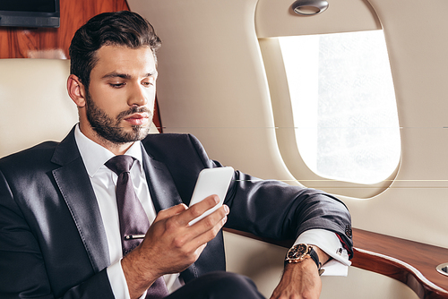 handsome businessman in suit using smartphone in private plane