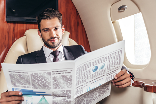 handsome businessman in suit holding newspaper in private plane