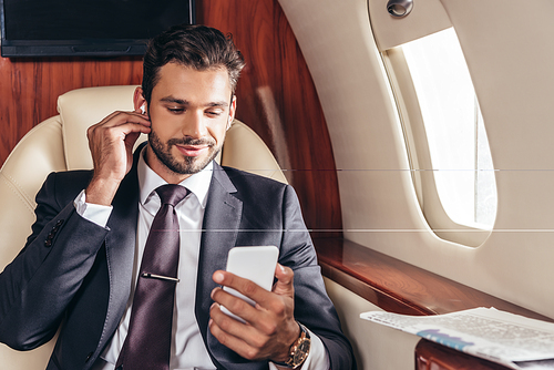 handsome businessman in suit listening music and using smartphone in private plane