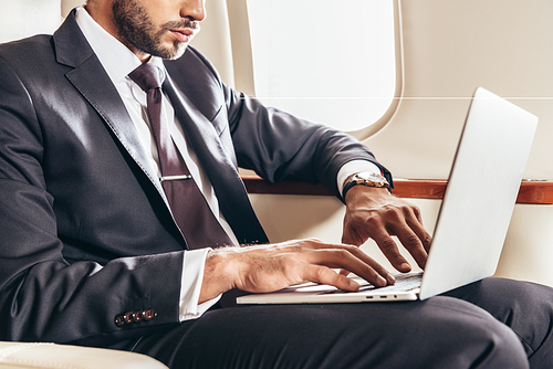 cropped view of businessman in suit using laptop in private plane