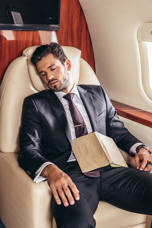 handsome businessman in suit with book sleeping in private plane