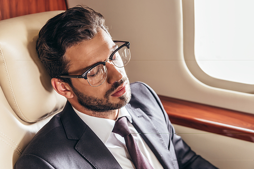 handsome businessman in suit and glasses sleeping in private plane