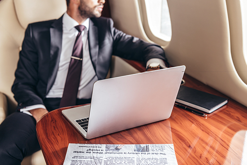 cropped view of businessman in suit and laptop on table in private plane