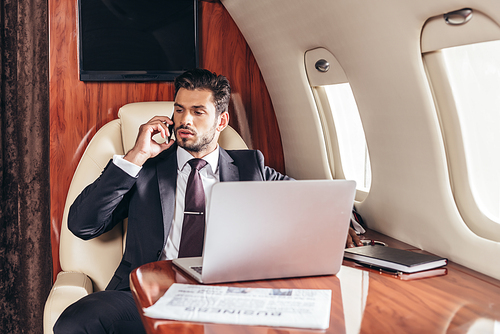 handsome businessman in suit talking on smartphone in private plane