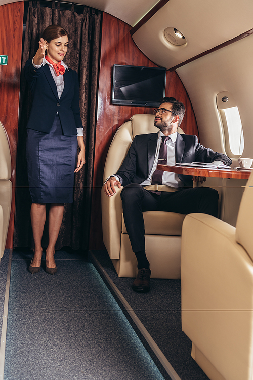 flight attendant showing gesture to handsome businessman in suit in private plane