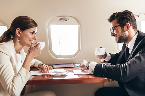 smiling businessman and businesswoman drinking coffee in private plane