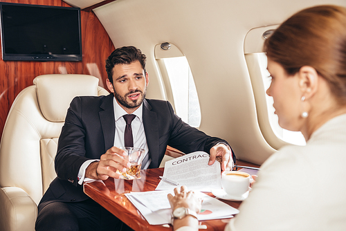 businessman with glass showing contract to businesswoman in private plane