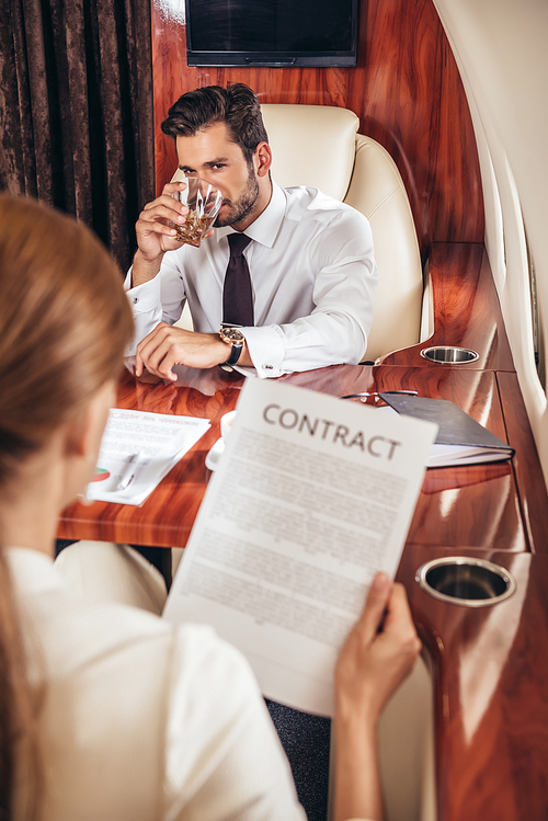 selective focus of businessman looking at businesswoman with contract in private plane