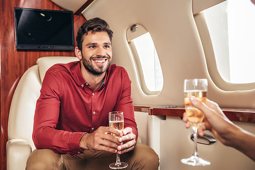 smiling boyfriend and girlfriend holding champagne glasses in private plane