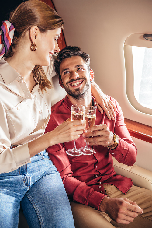 smiling boyfriend and girlfriend clinking with champagne glasses in private plane