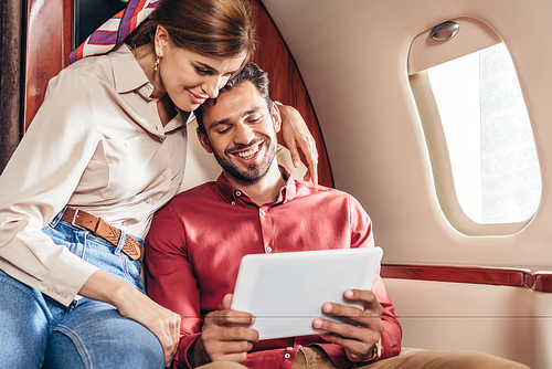 smiling boyfriend and girlfriend looking at digital tablet in private plane