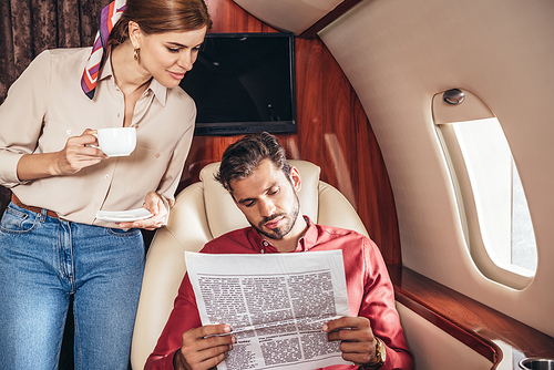 boyfriend and girlfriend with cup reading newspaper in private plane