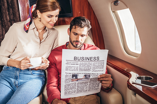 boyfriend and girlfriend with cup reading newspaper business in private plane