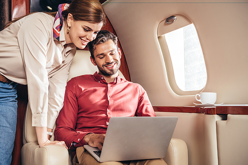 smiling boyfriend and girlfriend looking at laptop in private plane