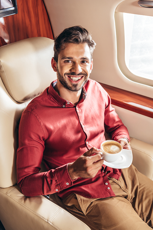 handsome man in shirt smiling and holding cup in private plane