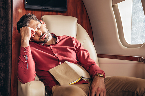 handsome man in shirt sleeping with book in private plane