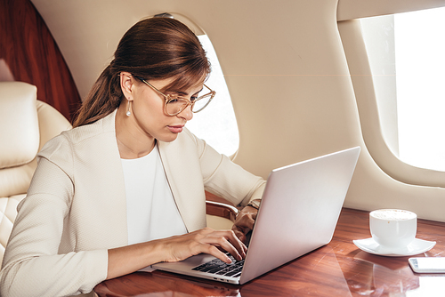 attractive businesswoman in suit using laptop in private plane