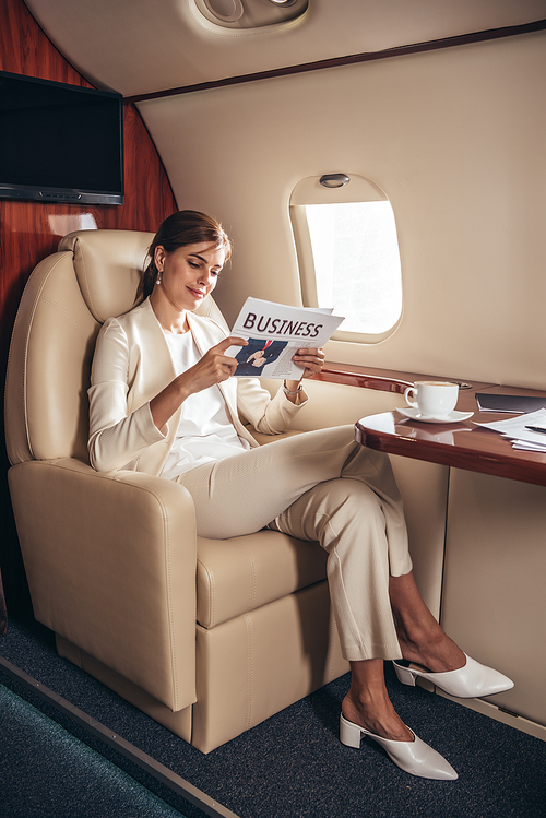 smiling businesswoman in suit reading newspaper business in private plane