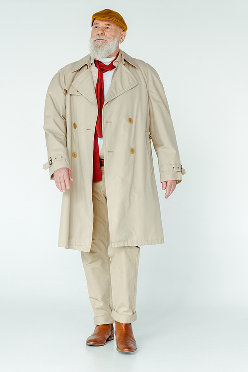 Full length of stylish senior man in trench coat looking away on white background