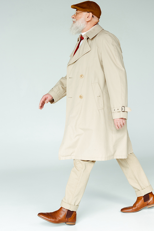 Side view of handsome senior man in coat walking on white background