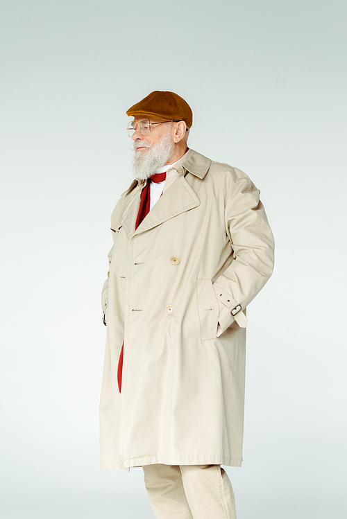 Handsome elderly man in trench coat and eyeglasses looking away isolated on grey