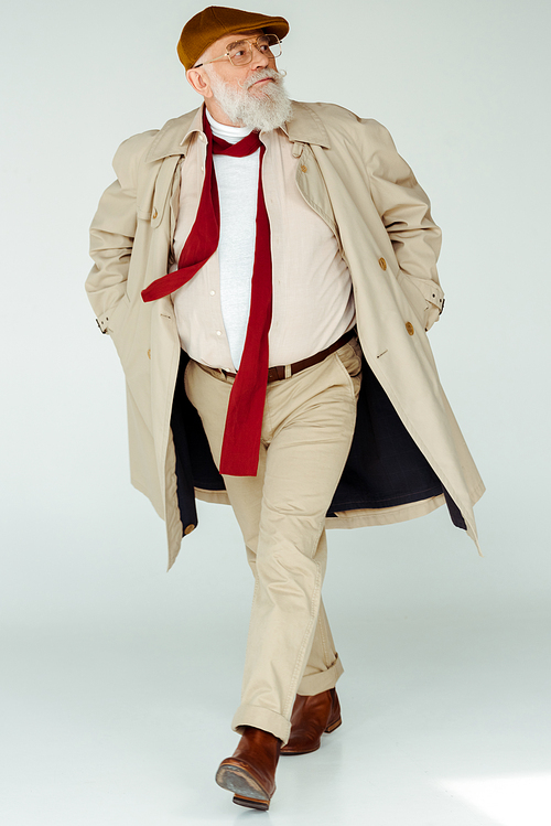 Full length of handsome senior man in trench coat walking on white background