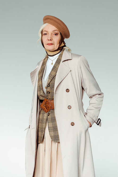 Fashionable senior woman in beret and trench coat  isolated on grey