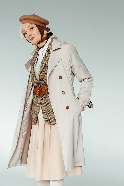 Elegant senior woman with hand in pocket of trench coat  isolated on grey