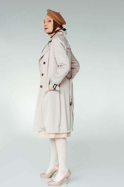 Side view of stylish senior woman in trench coat  on white background