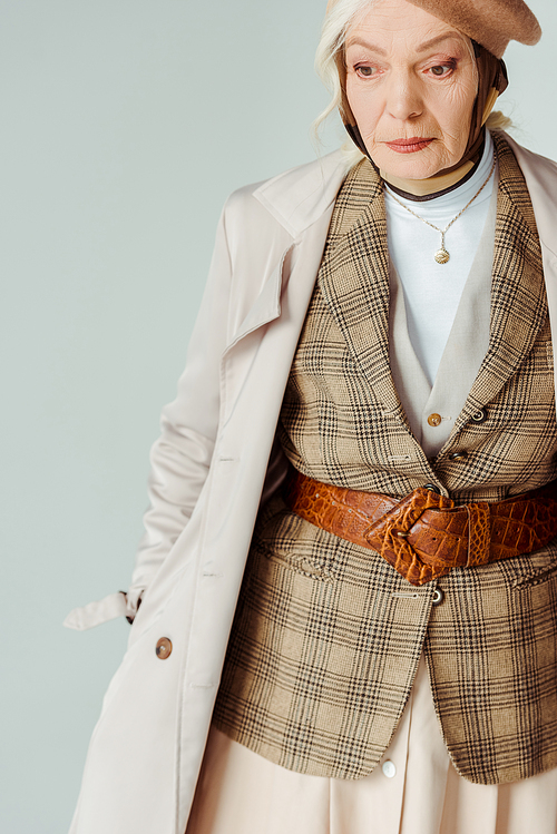 Fashionable elderly woman in trench coat looking away isolated on grey